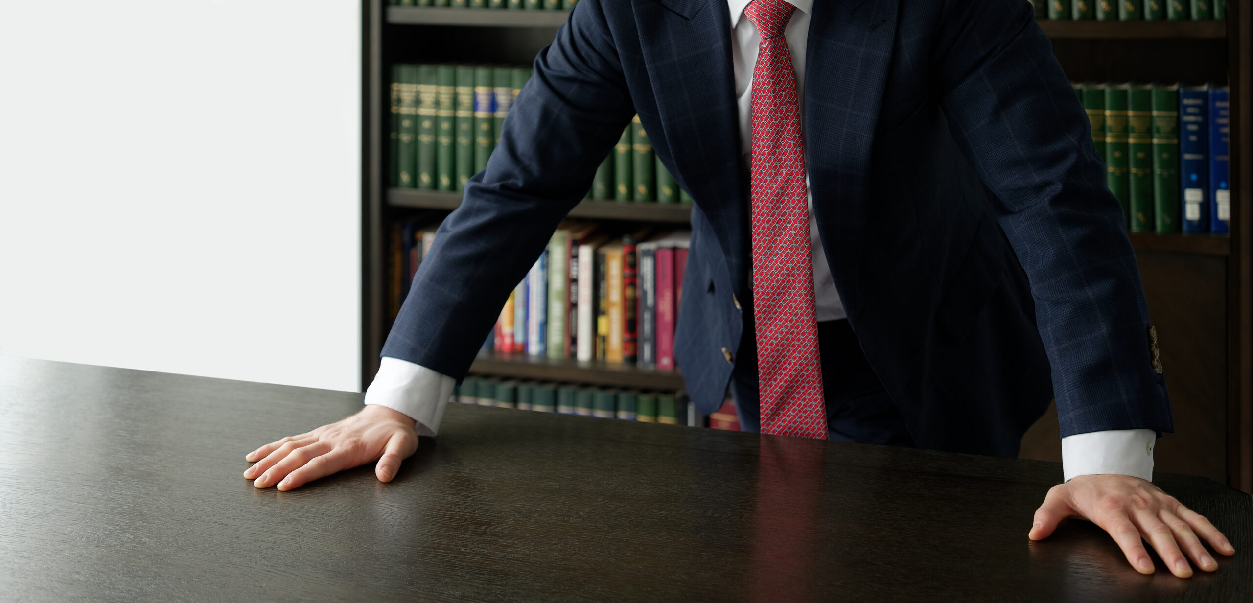 Close up of male hands on table, businessman In dark blue suit standing near table, leaning his hands on table, shelves with professional books in background, copy space
